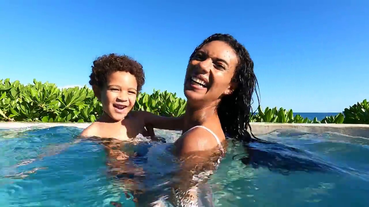 在热带度假胜地，微笑的母亲抓住儿子在游泳池玩的中近镜头视频素材