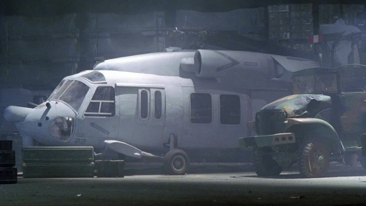直升机在军用补给仓库爆炸的广角镜头，伪装吉普车驶过。吉普车和直升机机身在火焰中燃烧。烟。视频下载
