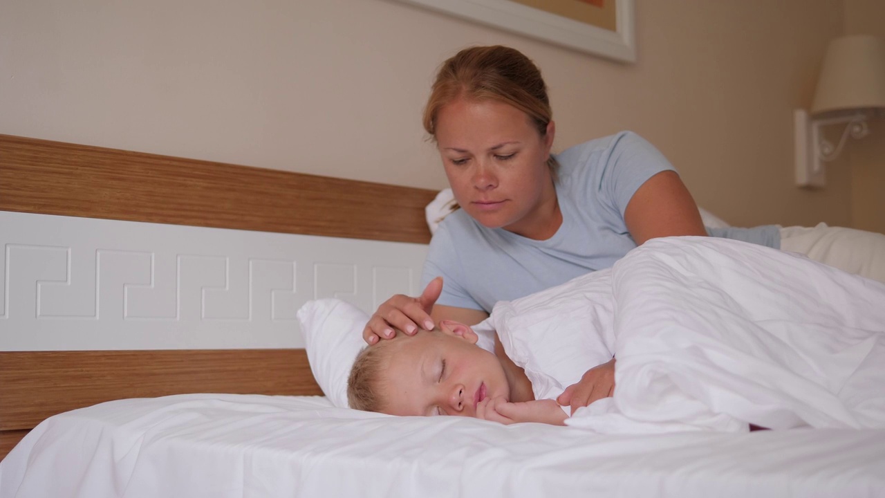 一位母亲的肖像，她羡慕她的小儿子，谁睡在床上的早上视频素材