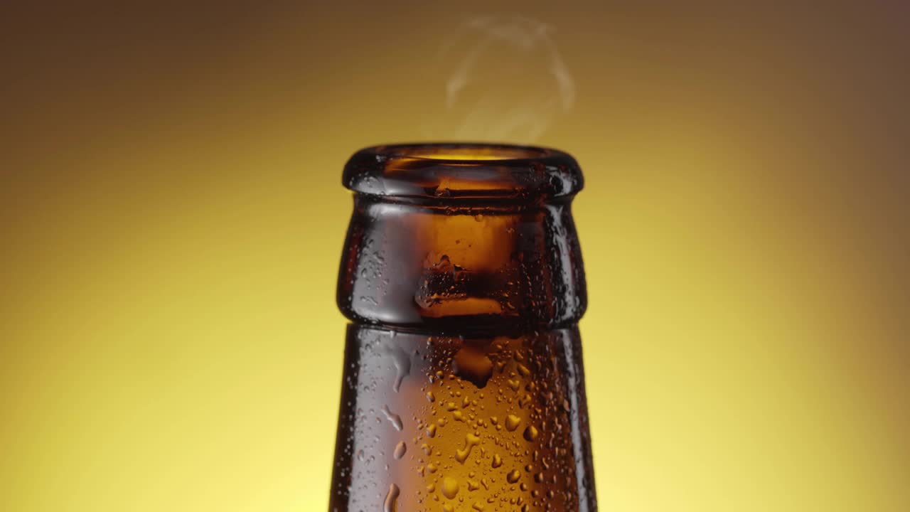 随着镜头，啤酒慢慢滴下雾蒙蒙的啤酒瓶。黄色背景。视频素材