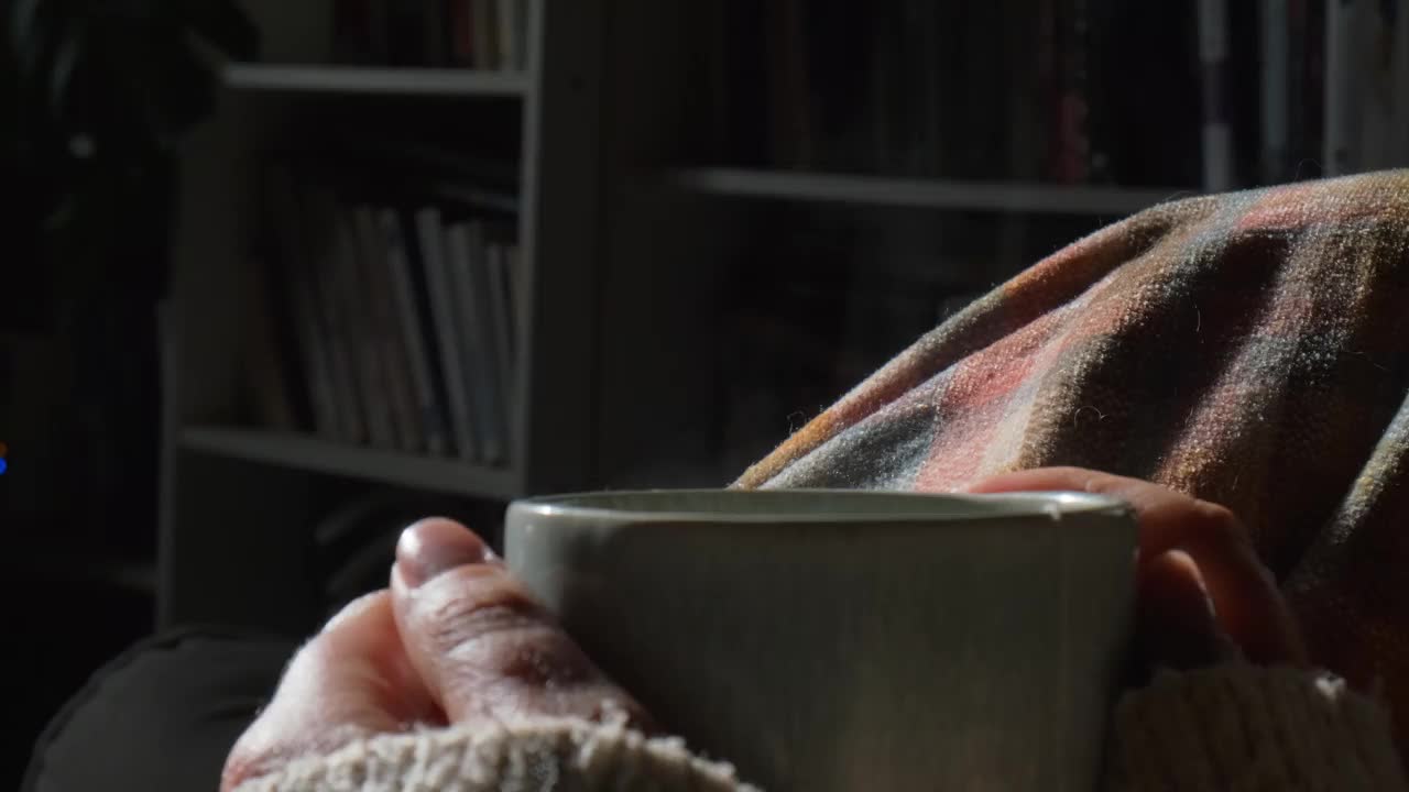 一个女人的手在一个舒适的室内环境与格子花呢喝热花草茶的特写视频下载