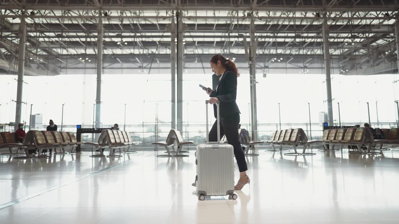年轻的女商人走在机场航站楼时使用智能手机视频素材