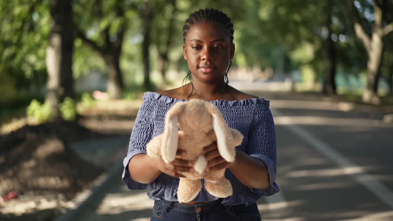 快乐的千禧一代非裔美国妇女欣赏站在阳光公园户外的玩具兔子。肖像积极美丽的大码女士享受夏天的周末在慢动作。视频素材