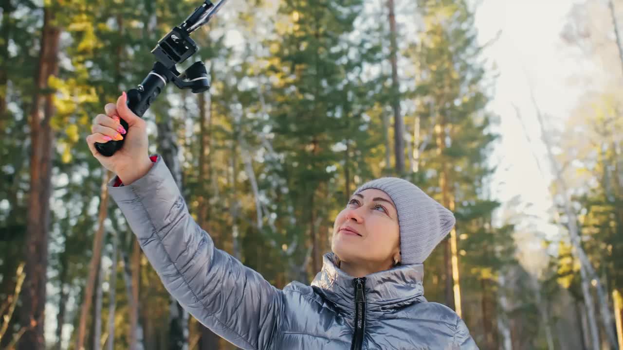 女人在冬天手持电影3轴万向节稳定装置的智能手机。视频摄影师操作员拍摄照片视频视频下载