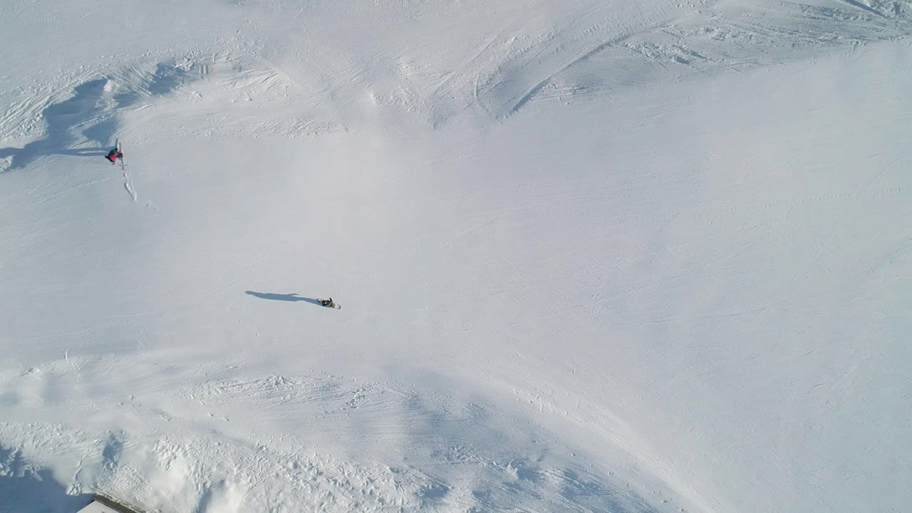 在晴朗的冬日，滑雪板运动员沿斜坡向下滑行至滑雪缆车底部站的鸟瞰图视频素材