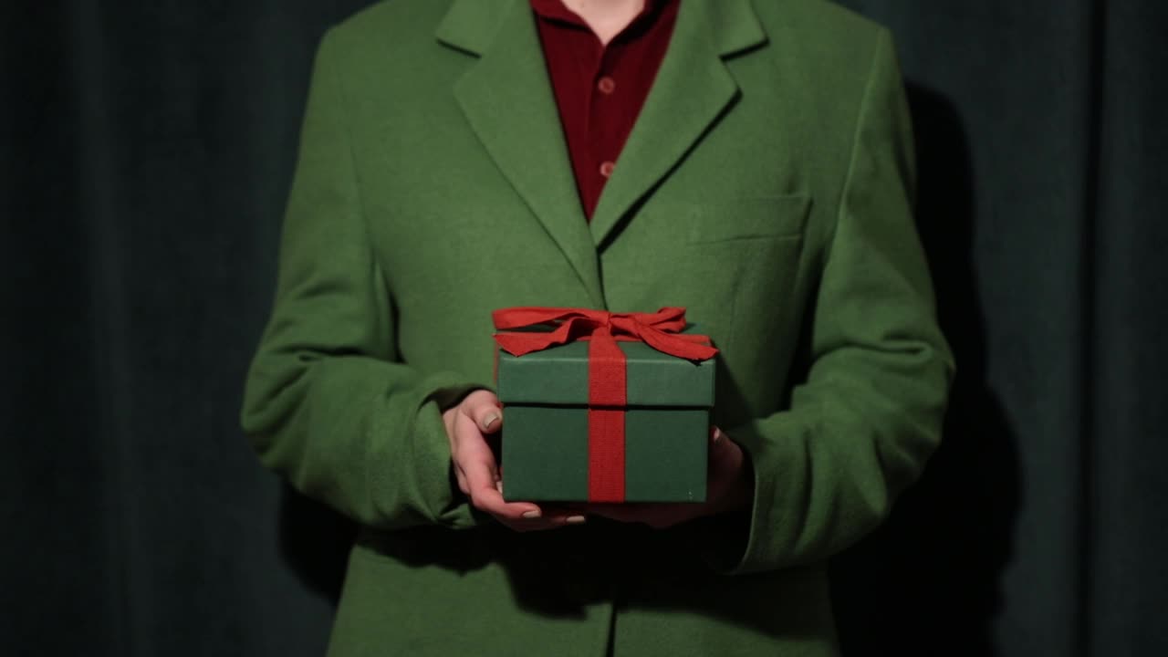 穿着绿色运动上衣的女人拿着绿色窗帘上的礼品盒作为背景视频下载
