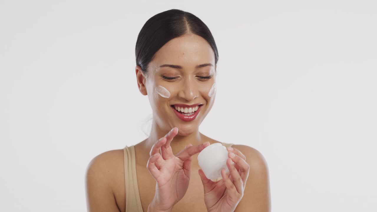一个美丽的年轻女子在脸上涂润肤霜的4k视频片段视频素材