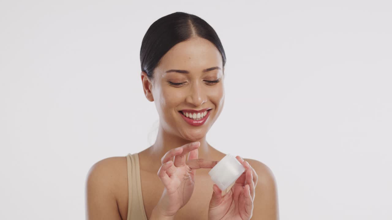 一个美丽的年轻女子在脸上涂润肤霜的4k视频片段视频素材