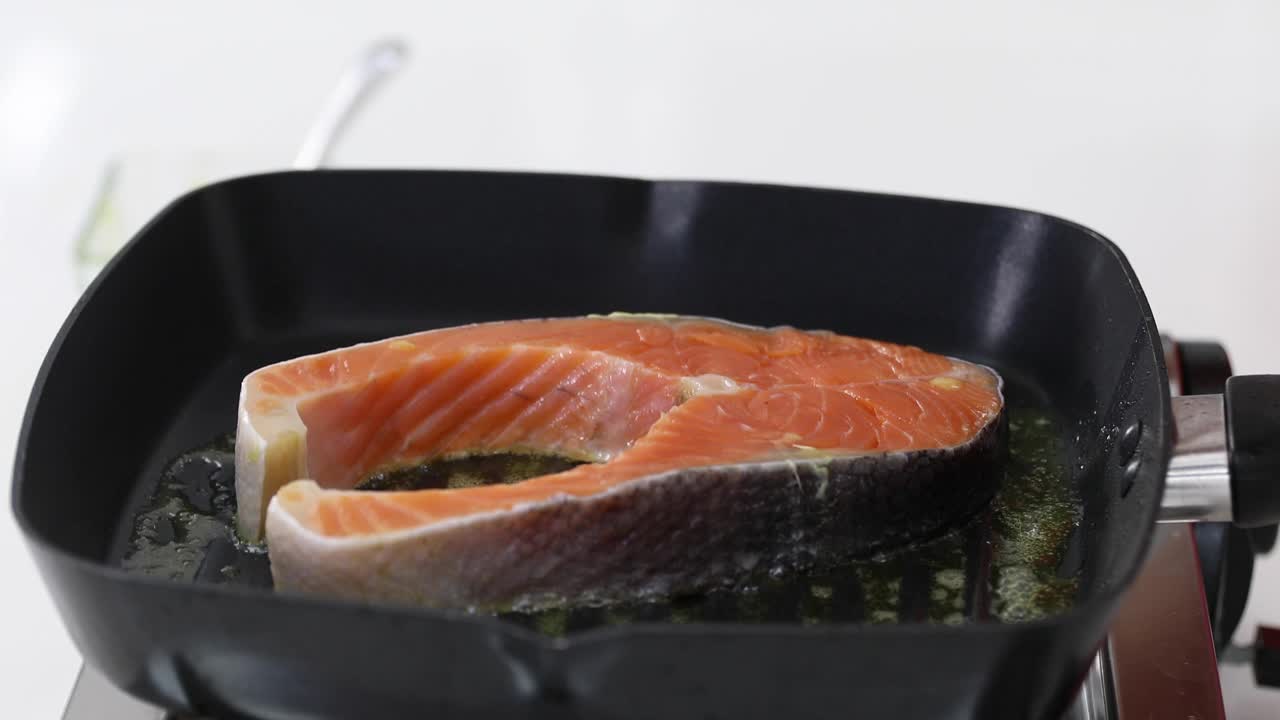 一大块新鲜的鱼放在热的金属锅上，用来做鱼排。视频下载
