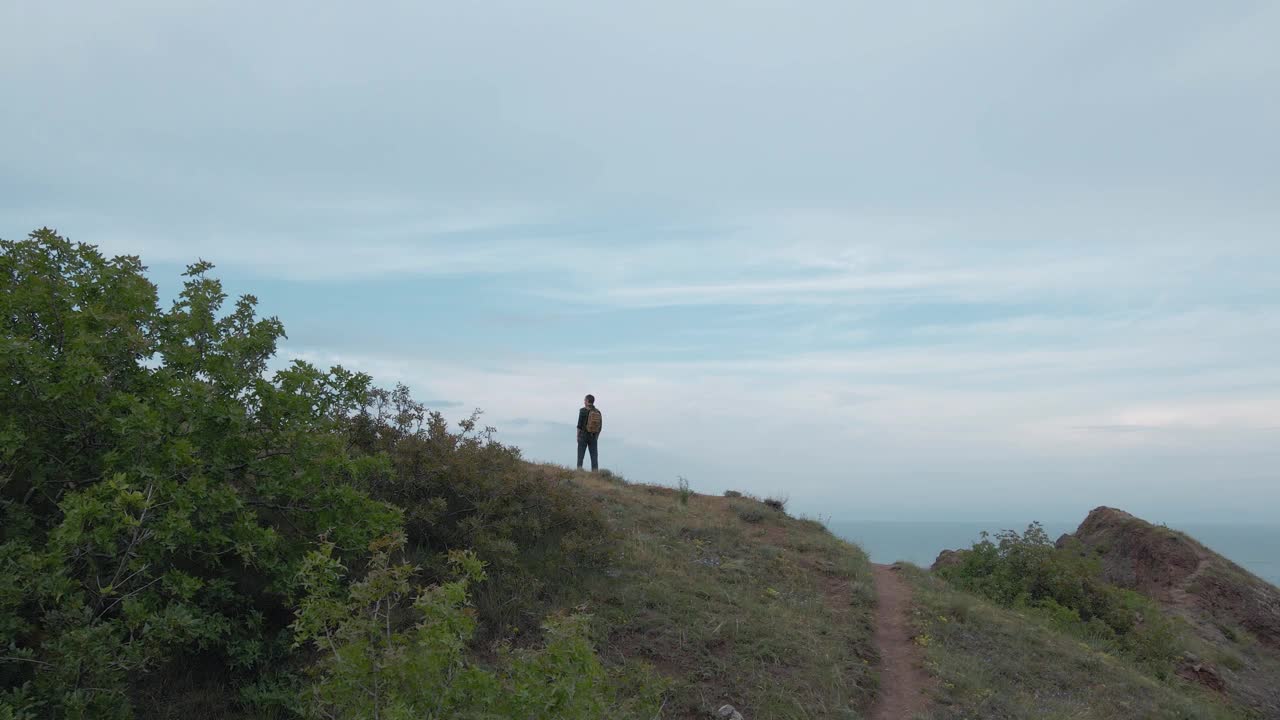 航空摄影无人机视图积极徒步旅行的人与背包站在岩石山附近的蓝色的海与天空地平线在户外休闲娱乐活动冥想视频下载