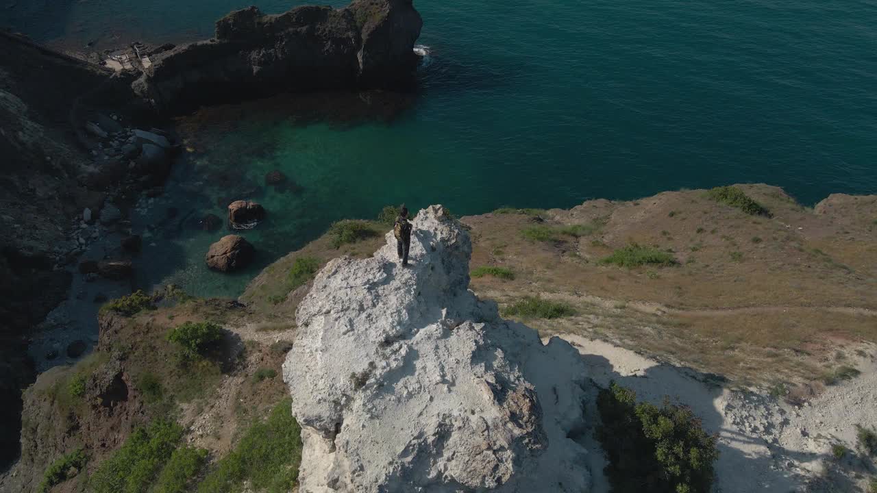 空中旋转无人机主动徒步旅行的人站在岩石山附近蓝色的海与天空地平线以上的美丽海湾在户外休闲娱乐活动视频下载