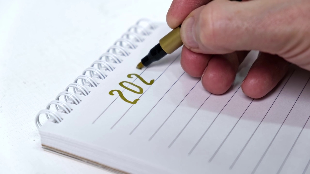 一名男子用金毡尖笔在笔记本上写下2022年的数字。视频下载