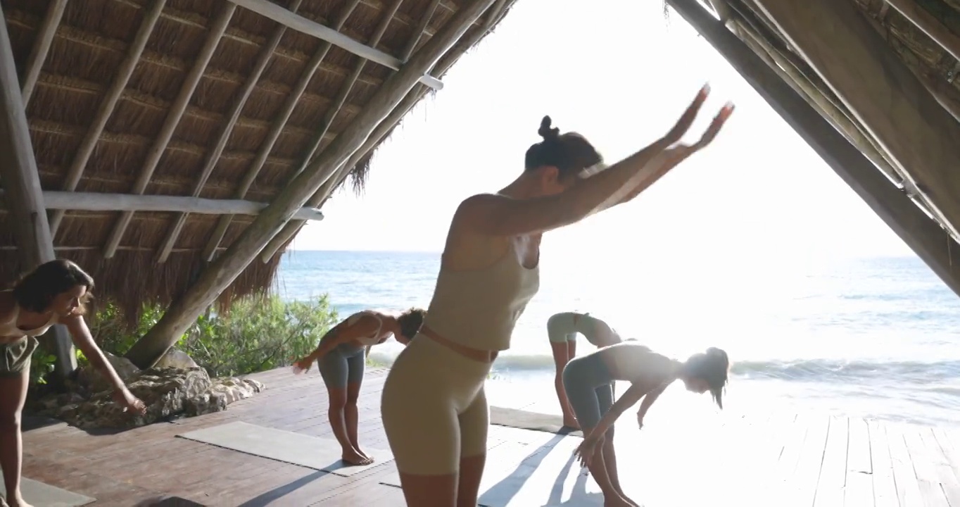 在热带度假胜地的海滨凉亭练习瑜伽时，妇女移动到战士姿势的中特写镜头视频素材