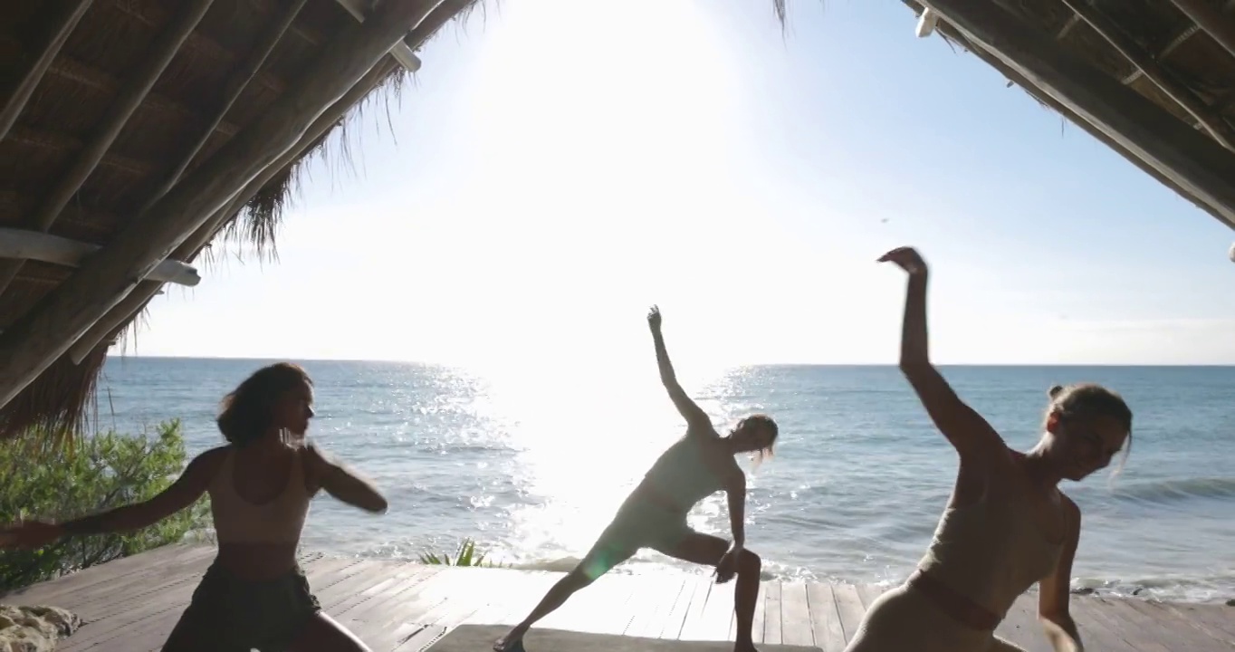 在热带度假胜地的海滨凉亭，在瑜伽课上，妇女们移动到延伸的侧角姿势的广角镜头视频素材