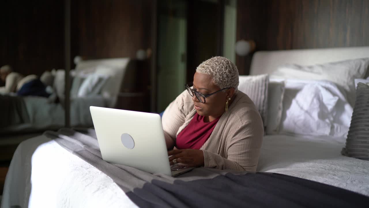 成熟的女人在家里的床上使用笔记本电脑视频素材