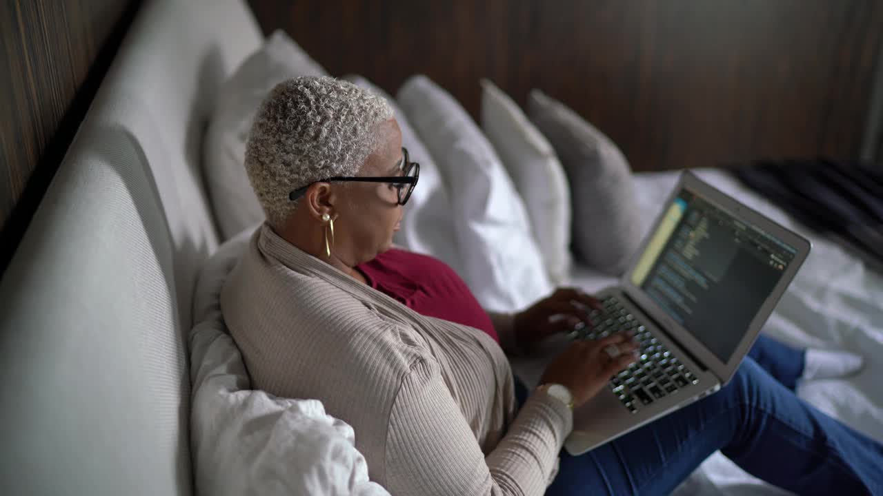 一个成熟的女人在家里的床上使用笔记本电脑视频素材