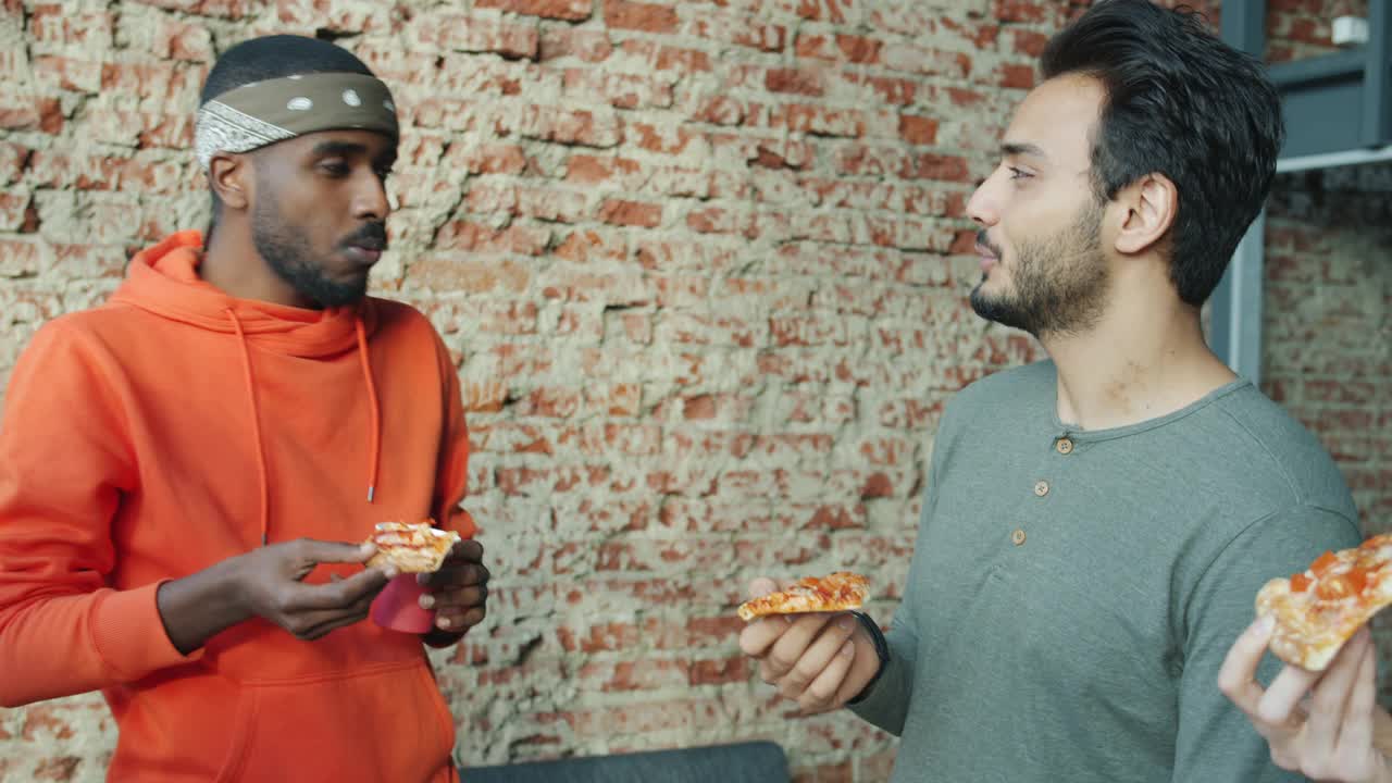 非裔美国人和阿拉伯商人在现代办公室里吃披萨，聊天视频素材