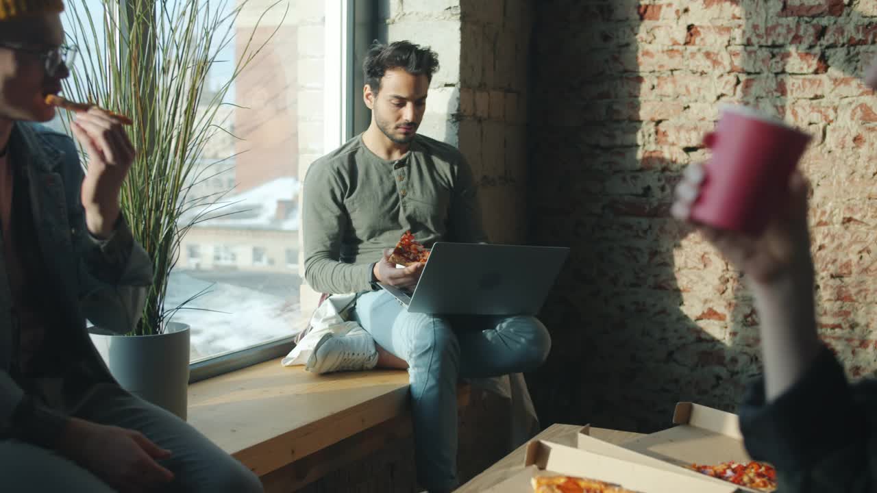 在办公室吃着披萨，在白天用笔记本电脑聊天的各种各样的商人视频素材