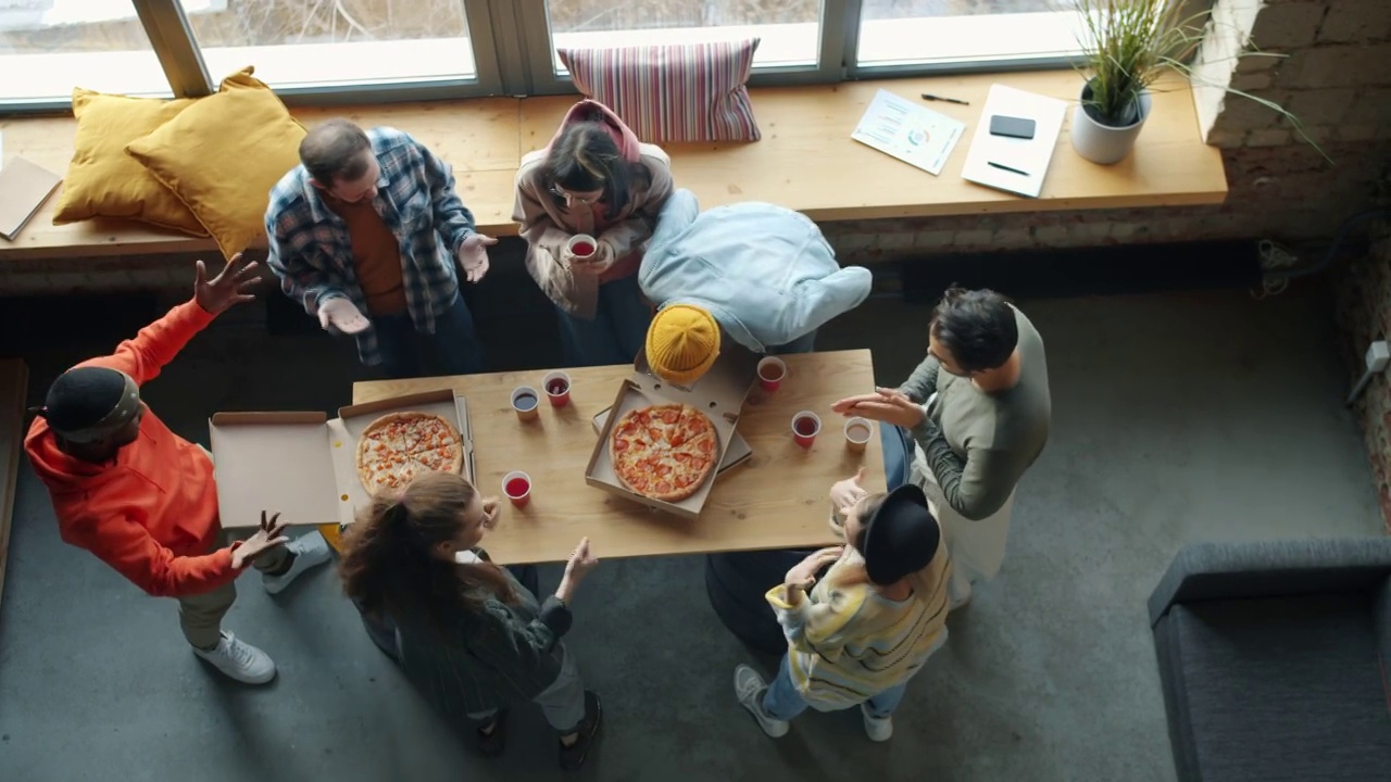俯视图快乐的同事带着披萨到办公室享受美味的食物鼓掌视频素材