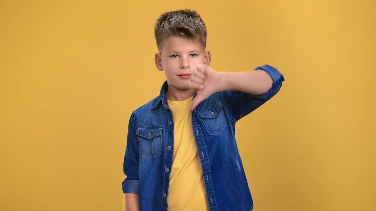 时髦的男性青少年的肖像显示拇指向下皱眉摇头摆姿势孤立在橙色视频下载
