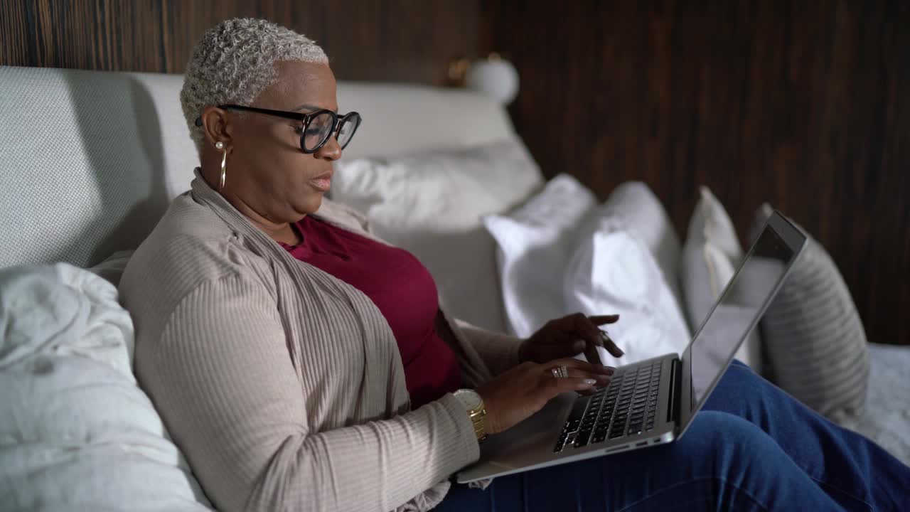 一个成熟的女人在家里的床上使用笔记本电脑视频下载