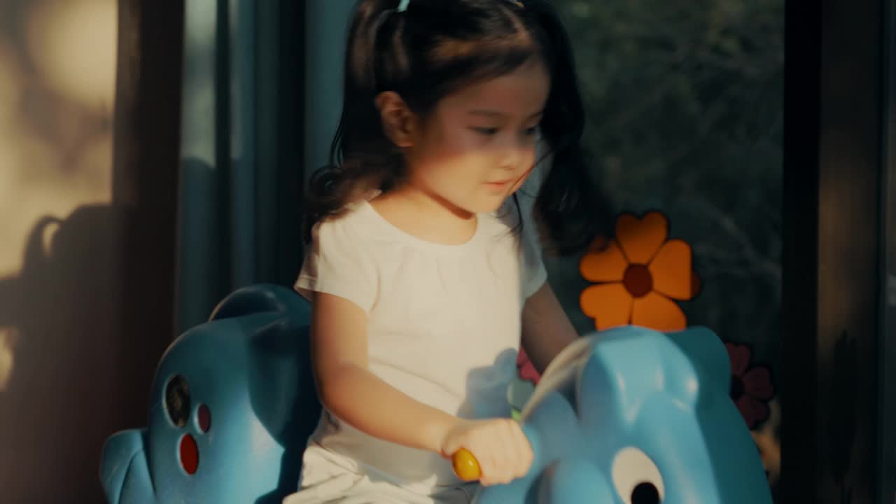 可爱的女孩骑玩具马在阳光的游戏室视频下载
