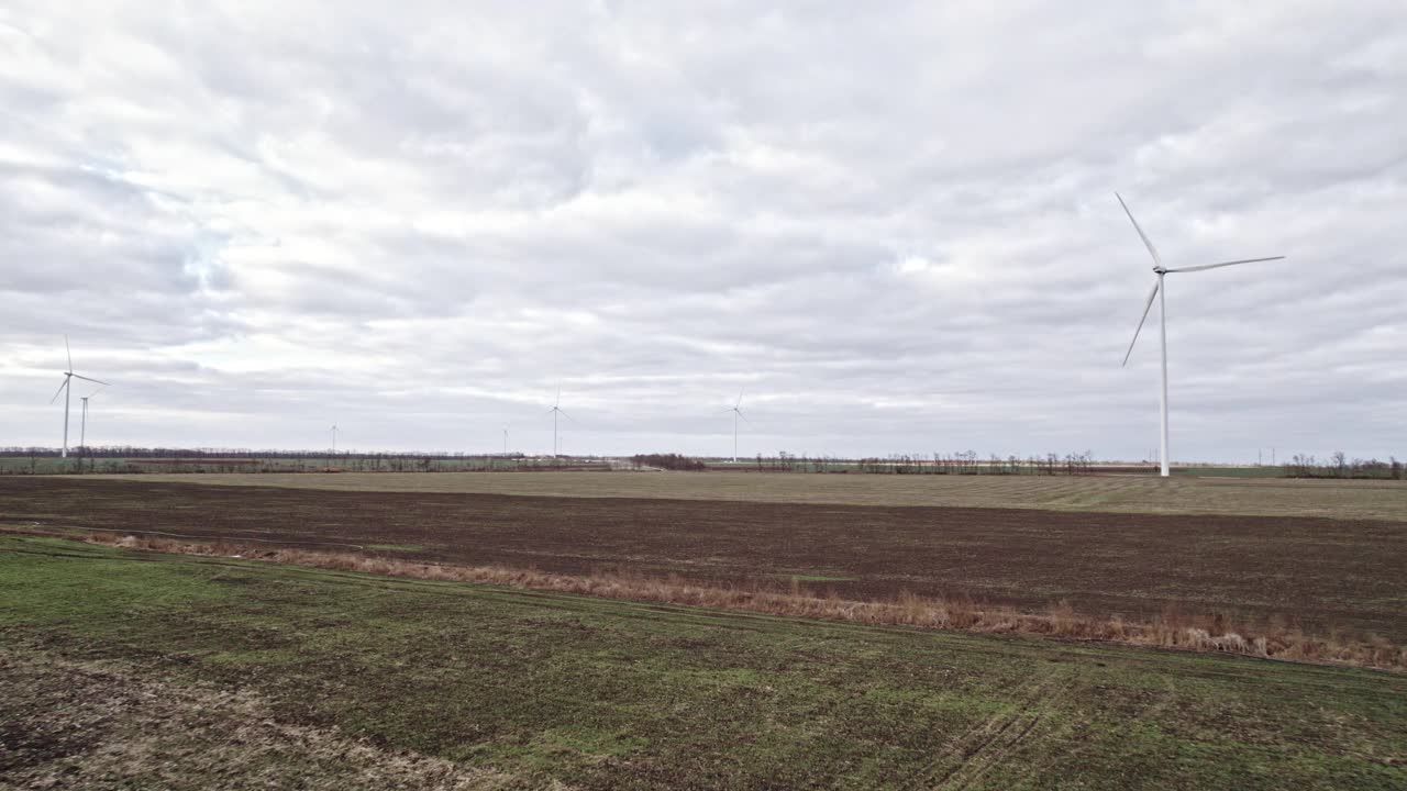 在田间的大农场全速转动叶片。旋转的风车在灰色的天空背景。由风力涡轮机产生的清洁可再生能源。另一种生活方式视频素材