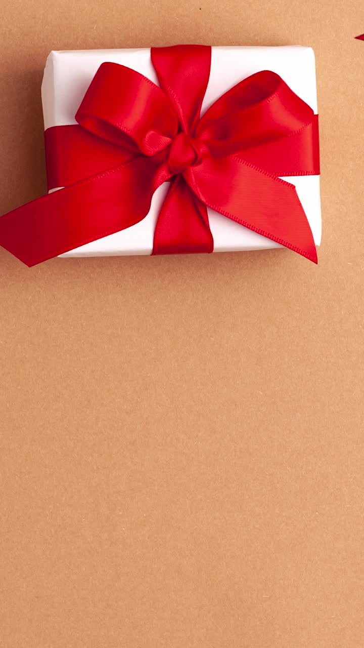 人的双手用红色的袖子带走白纸上的礼物，用红色的缎子丝带蝴蝶结在棕色的背景上，红色的星星形状。停止运动垂直动画圣诞假期概念平lay视频素材