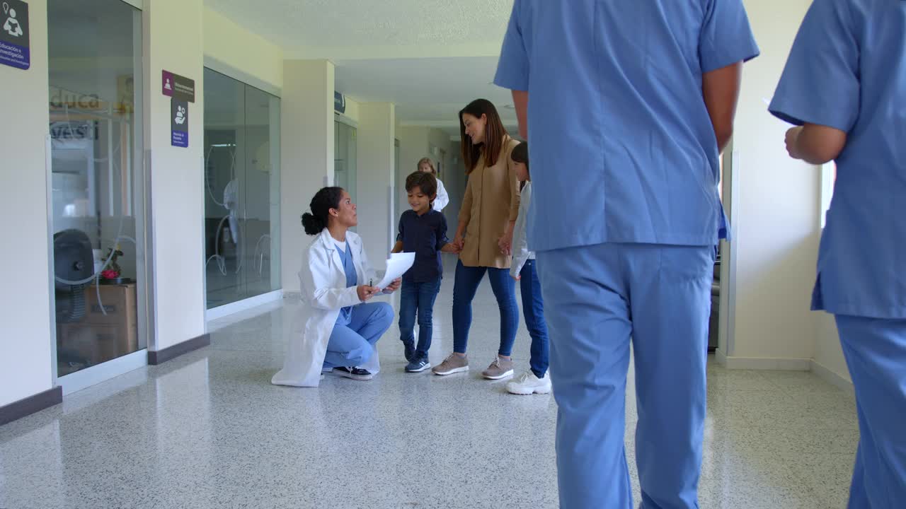 一名年轻的儿科医生在医院走廊与她的病人和母亲交谈，而其他医生和护士则从旁边走过视频素材