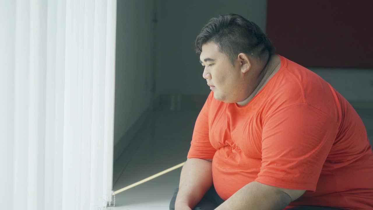 一个超重的男人坐在窗边沉思视频素材