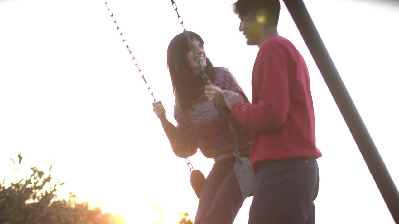 日落时分，一对年轻的情侣在荡秋千视频素材