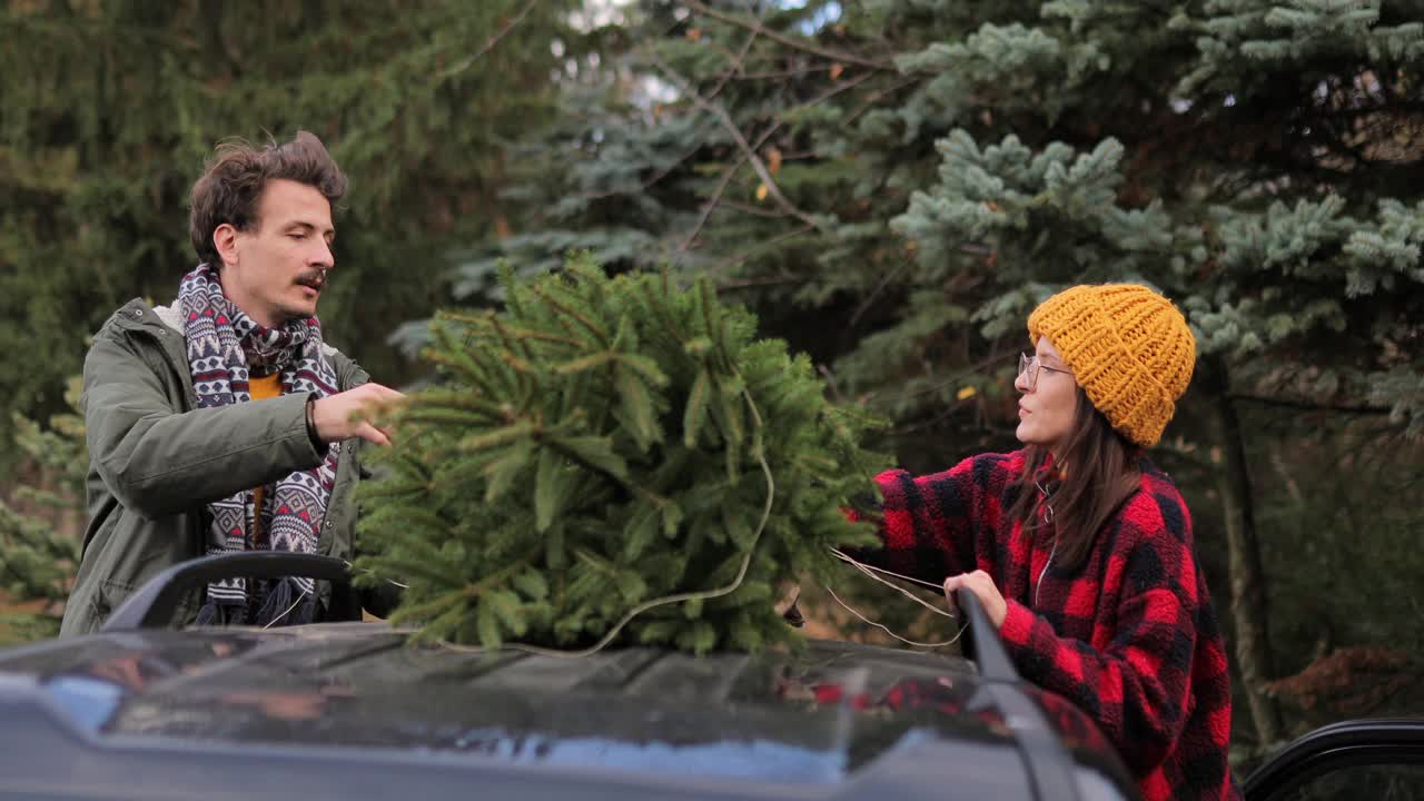 年轻夫妇把他们的新圣诞树绑在汽车屋顶上视频下载