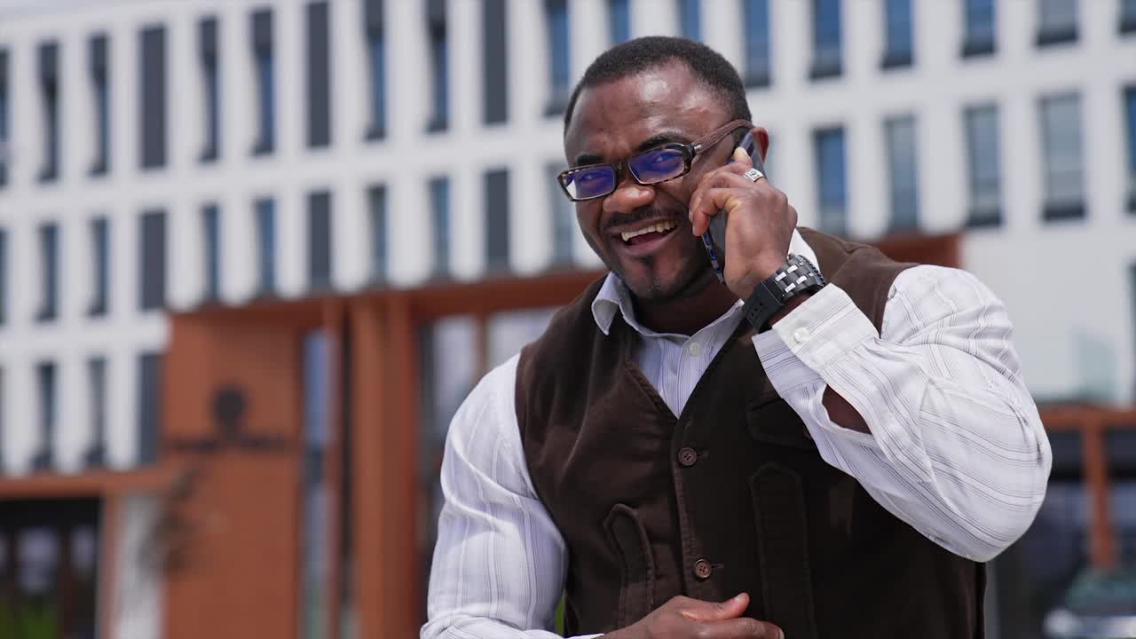 一个非洲男人，身材健美，在城市里打电话。成功的深色皮肤的商人在城市背景下进行电话交谈。视频下载
