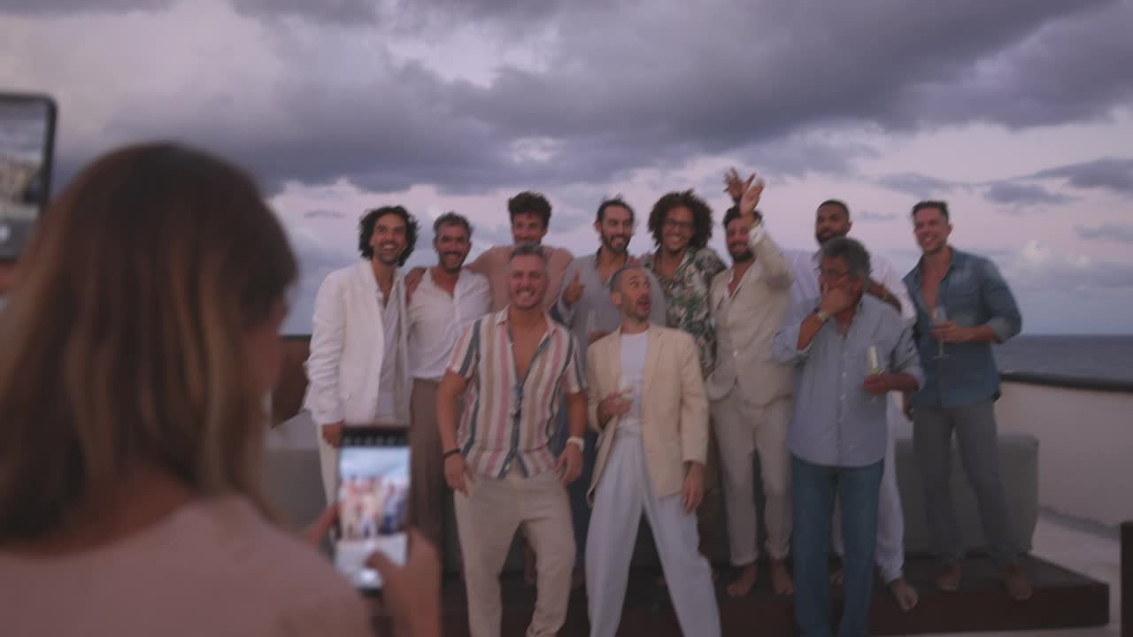 在热带度假胜地，在婚礼后的屋顶派对上，一名女子在拍摄新郎和朋友的照片视频下载