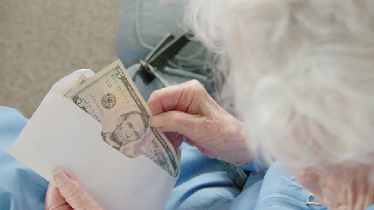 一位年长的白人妇女一边从信封里数钱，一边看着一张五美元钞票和一张一美元钞票视频下载