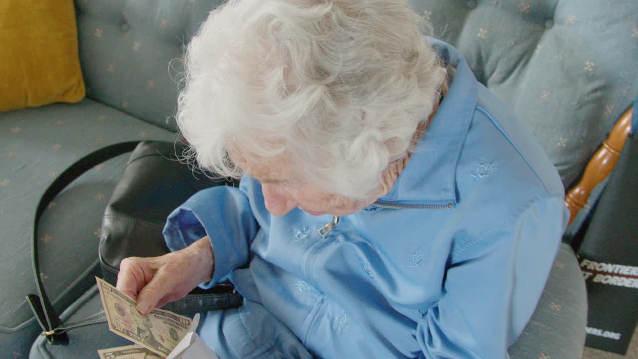 一位年长的白人妇女看着一张十美元的钞票，数着信封里的现金视频下载
