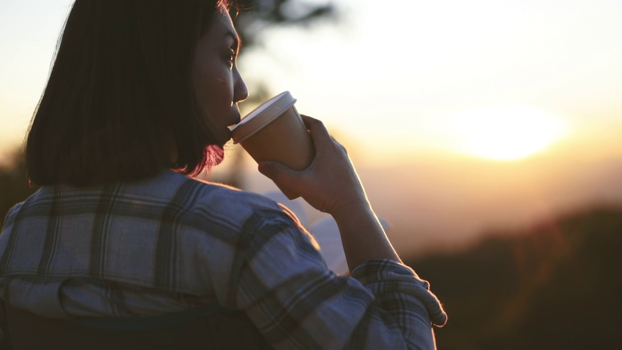 女人在户外，拿着咖啡杯在日落时分的山上放松视频素材