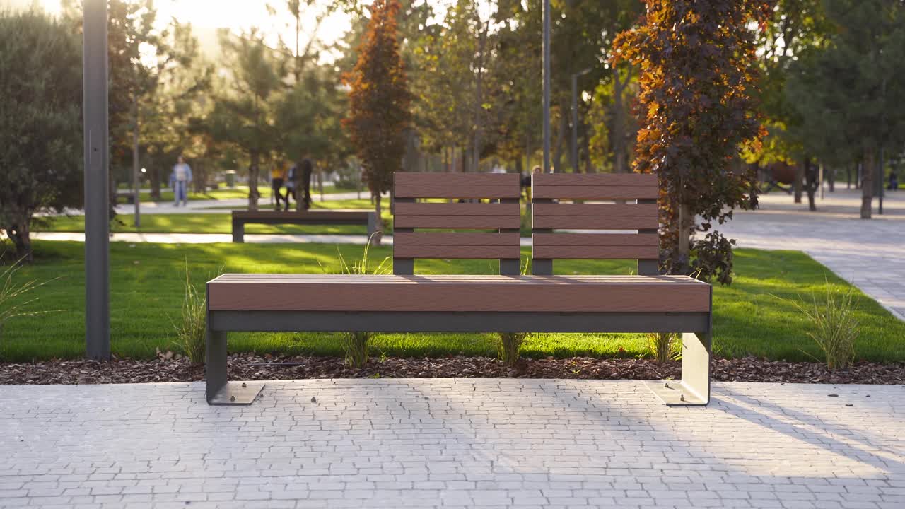 公园草坪上的现代木制长椅。时尚的新长椅在城市娱乐区日出或日落。城市主义主题公共空间景观设计。空荡荡的人行道上没有人视频下载