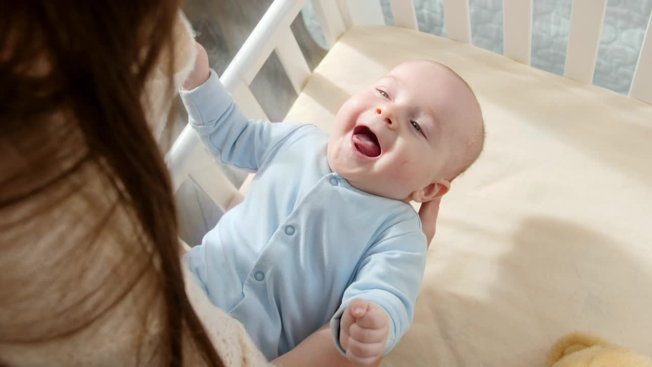 快乐的微笑的婴儿看着妈妈在摇篮里摇他。育儿观念、家庭幸福与宝宝成长视频素材