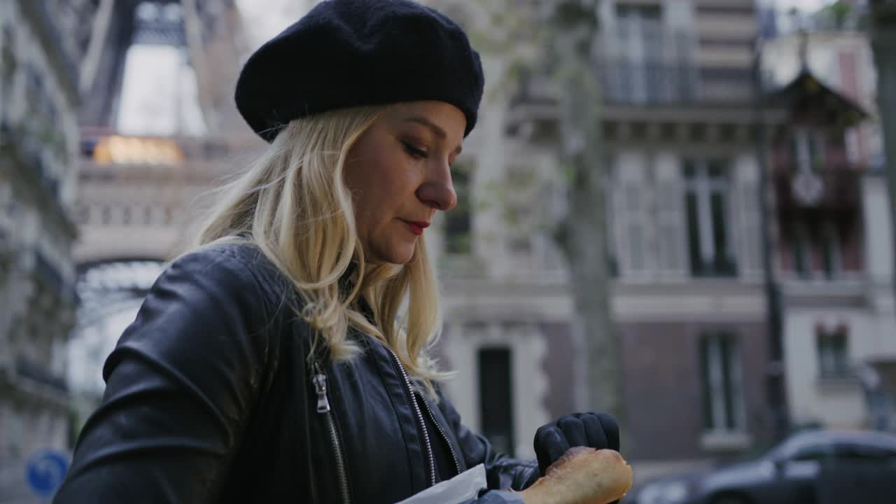 时尚的法国女人在埃菲尔铁塔旁的大街上吃法式长棍面包视频下载