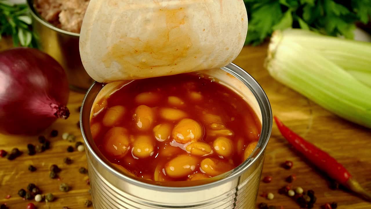 厨师用汤匙从厨房木板上的金属罐中取出番茄酱炖豆。视频下载