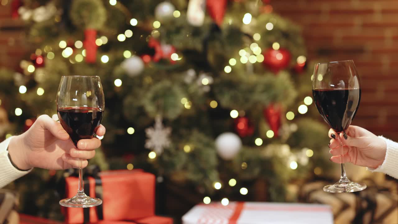 不知名的人们手捧酒杯，对着装饰着发光花环的圣诞树欢呼。模糊背景,散景。新年快乐。近景，慢镜头，4k视频下载
