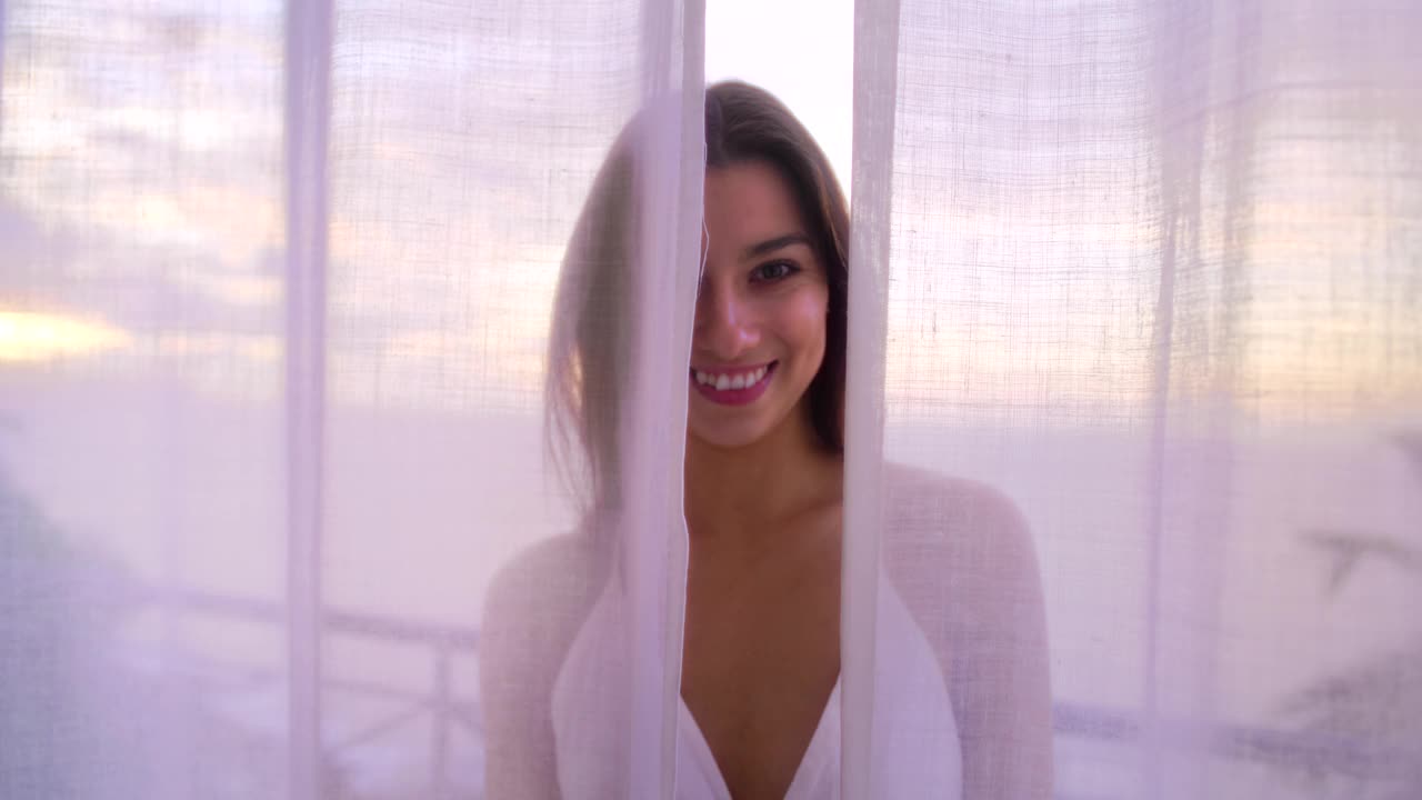 妩媚的女人躲在透明的窗帘后面。肖像视频素材