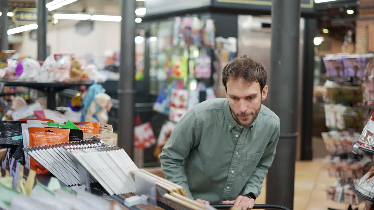 一个男人走过超市，从货架上拿了巧克力。阅读标签和成分视频素材