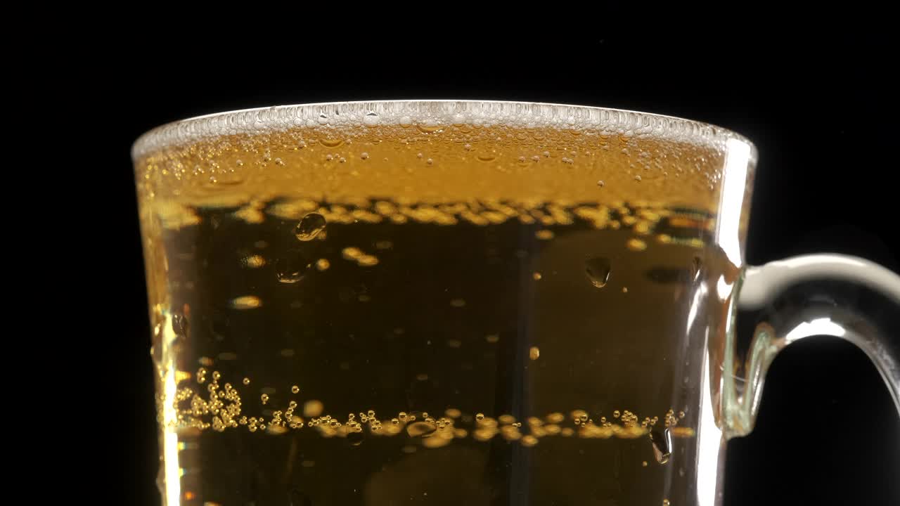 在黑色的背景下，将金色的啤酒从瓶子倒在品脱玻璃上视频素材