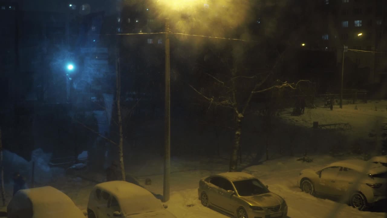 下雪的院子里，停车场里，路灯照亮。坏天气。汽车上到处都是雪视频素材