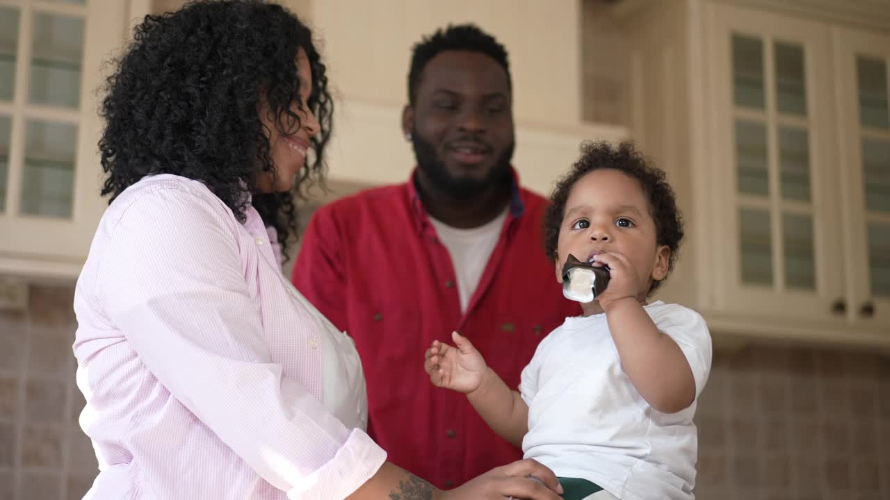 可爱的小非洲裔美国男孩吃儿童食品从管夫妇微笑爱的父母在厨房谈话。迷人的孩子像母亲和父亲欣赏孩子的品味。视频素材