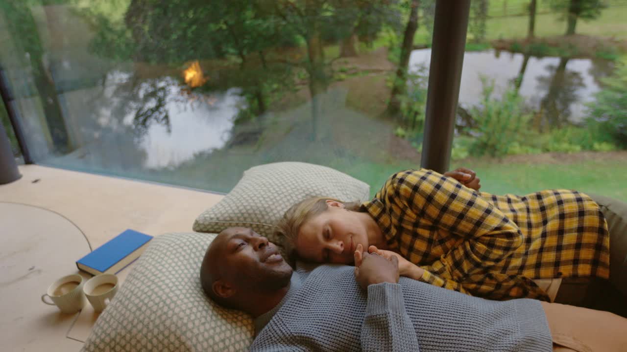 英国德文郡蒂弗顿现代住宅里，一对微笑的夫妇躺在窗边视频素材