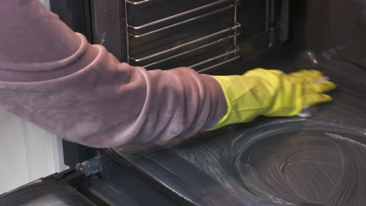 妇女戴着橡胶手套，用海绵清洁烤箱内部后，在厨房烹饪。视频素材
