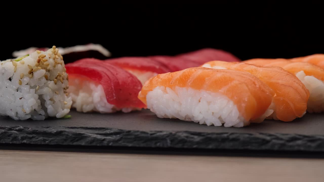 黑色背景的寿司在盘子上旋转。手握三文鱼，金枪鱼，寿司，浦隆町。典型的亚洲日本食物。视频下载